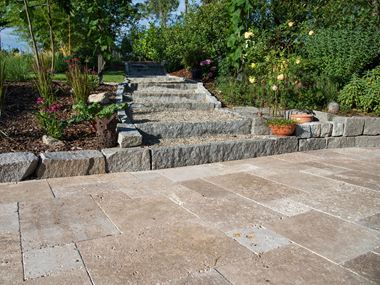 Travertin Noce als terrasbedekking, op de achtergrond leidt een pad naar een natuurlijke tuin