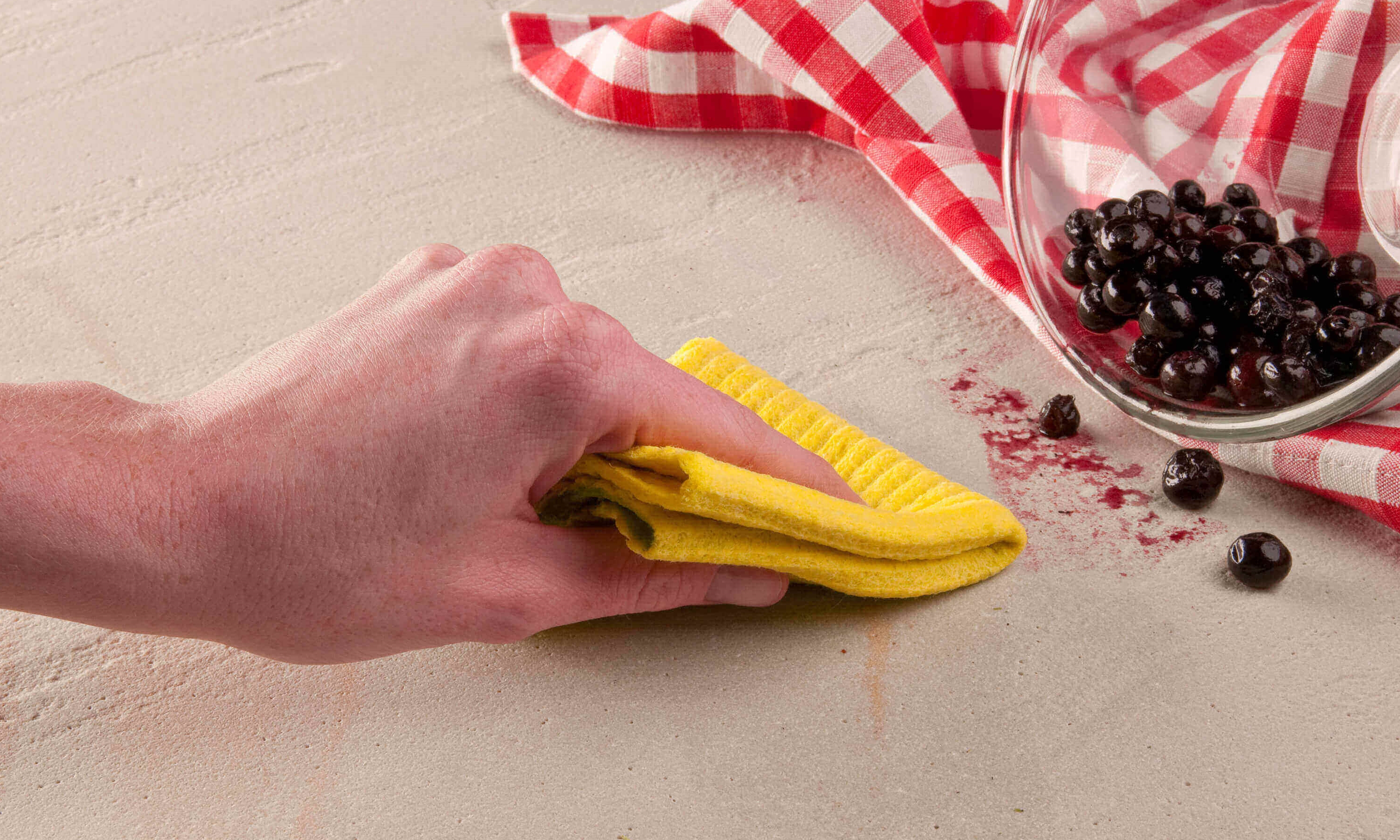 Hand veegt bessenvlek weg met gele doek