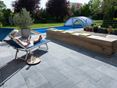 Een elegante steen voor een modern terras! Vrouw ontspant op een ligstoel op een terras met kalkstenen platen, op de achtergrond een tuin met zwembad