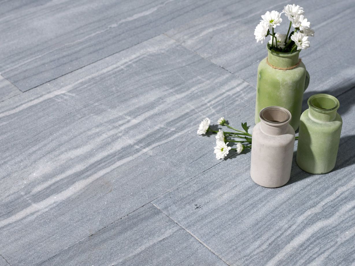 Facettenreiche Grautöne und feine Steinzeichnungen geben den Kalksteinplatten Ocean Grey den Look! Drie vazen met bloemen op kalkstenen platen in lichtgrijs met witte adering