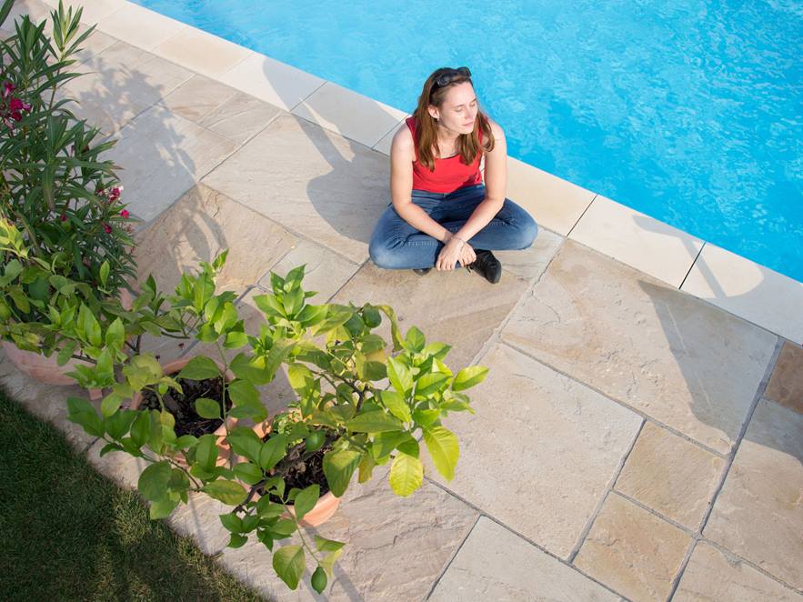 Vrouw zittend op zandstenen terras bij het zwembad van bovenaf gefotografeerd