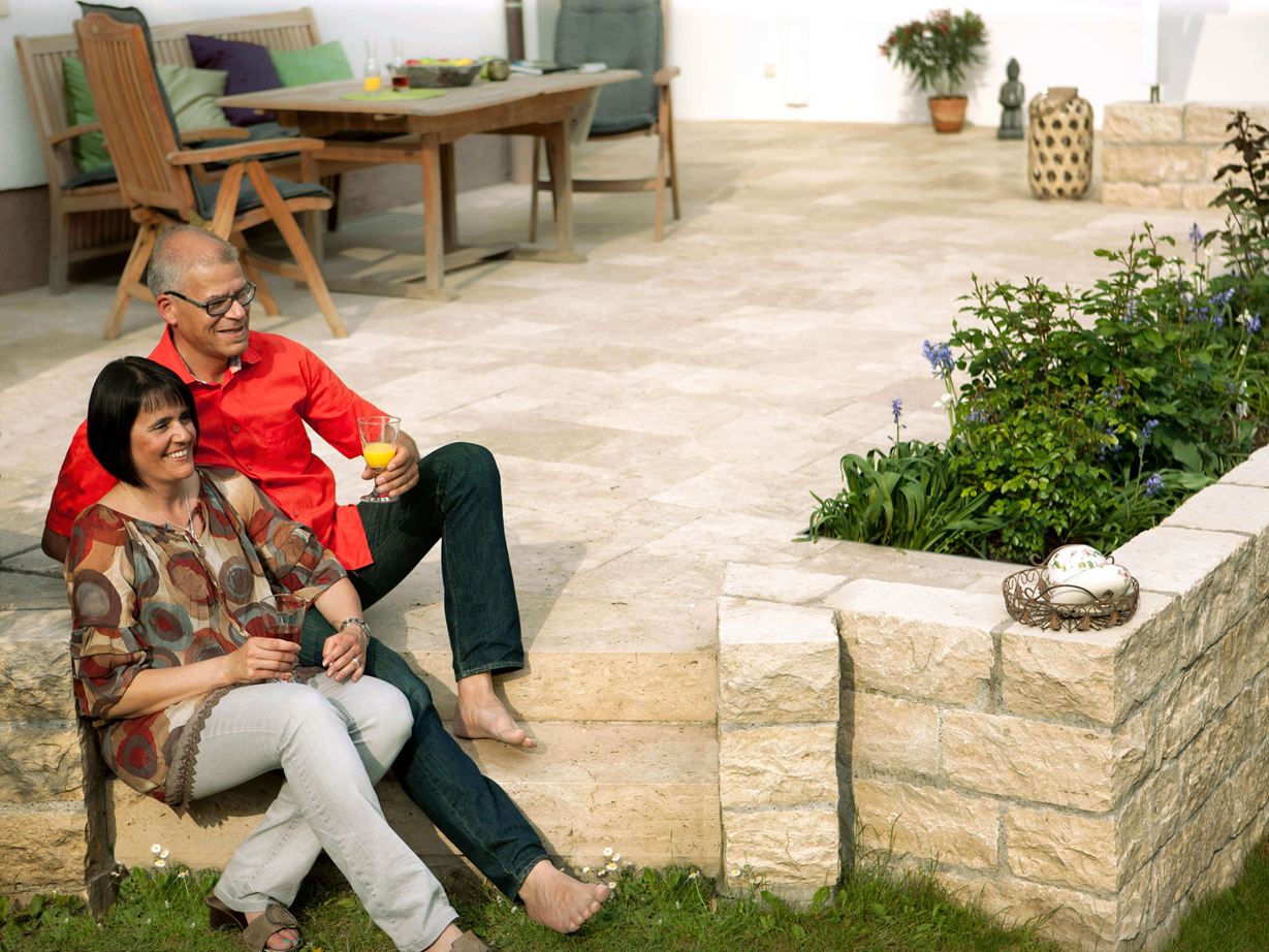 Een speciale traktatie voor blote voeten: travertin Echtpaar zittend op een terras met natuurstenen platen van Medium SELECT travertin en natuurstenen muur, houten tuinmeubilair op de achtergrond