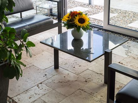 Levendig travertin combineert in beige in een moderne serre met glazen tafel en bloemenvaas
