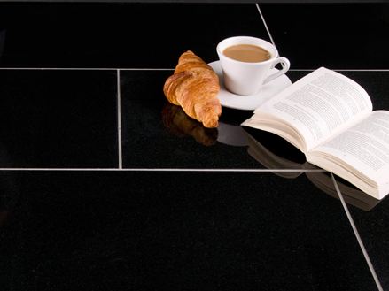 Kop koffie, croissant en een open boek op donkere granieten tegels met lichtgekleurd voegwerk