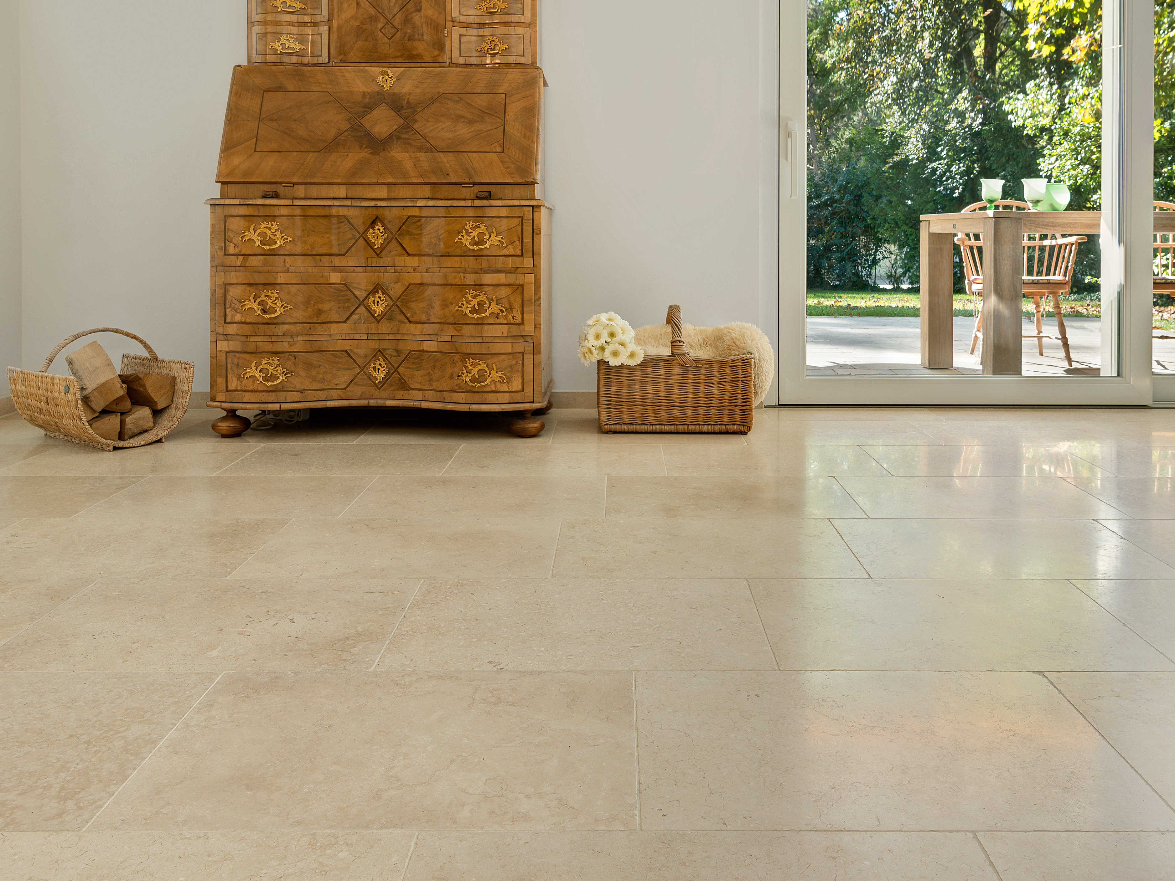 Harmonieuze beige tinten: Cleopatra Light kalksteen tegel Antieke houten kast op lichtgekleurde kalkstenen tegels Cleopatra Light, op de achtergrond zicht op het terras en de tuin