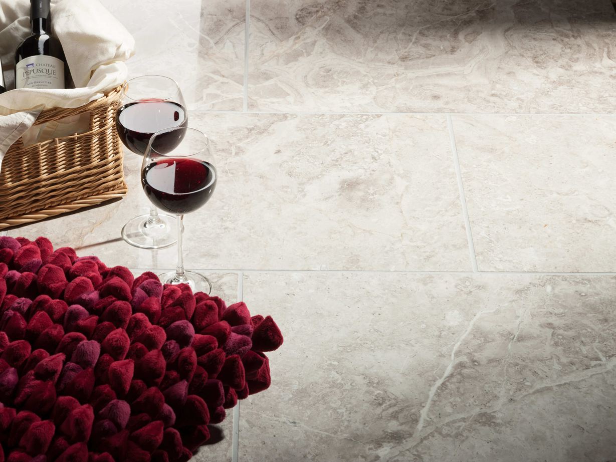 Twee wijnglazen staan naast mand met wijnfles en rood kussen op Silver Shadow gepolijste marmeren tegels