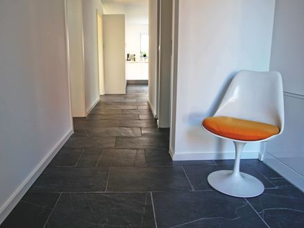 Klantenfoto: Zwarte Rustieke tegels in de gang met witte fauteuil op de voorgrond