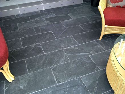 Rieten bed met rode kussens op donkere leistenen tegels Zwart Rustiek met witte voegen