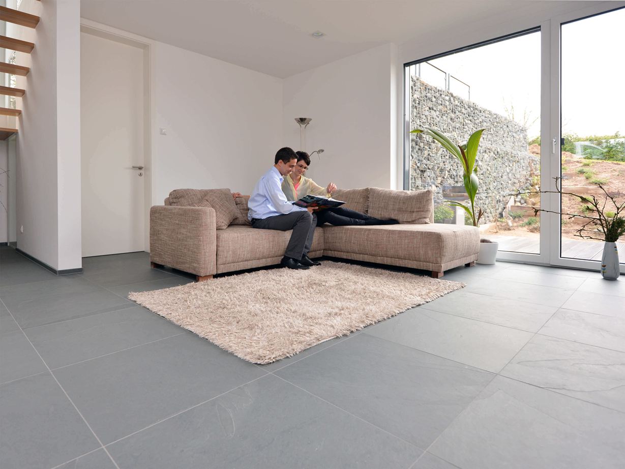 Grey Slate ziet er ruim en modern uit. Groot formaat Grey Slate leisteen tegel in de woonkamer met lichtgekleurde bank en witte muren. Een stel zit op de bank