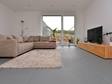 Woonkamer met beige bank, beige tapijt en houten tv-tafel op grijs leisteen in groot formaat