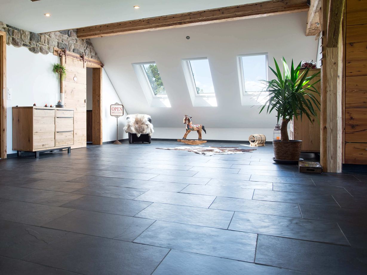 Der anthrazitfarbene Schiefer wirkt trendy. Kamer met antracietkleurige leistenen vloer en houten meubels, witte muren