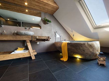 Rustieke badkamer met bad in steenlook en donkere leisteen tegels als vloerbedekking