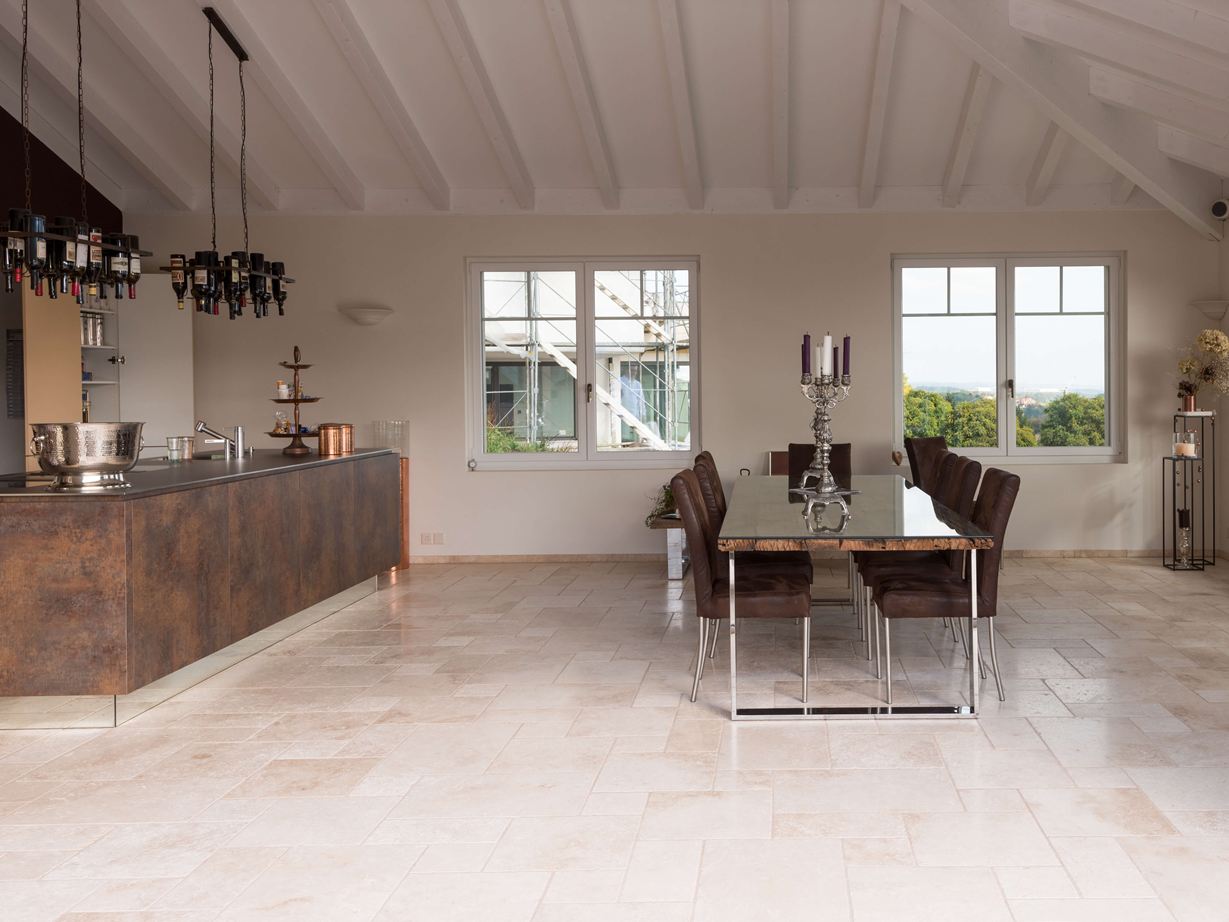 Moderne keuken ontmoet mediterrane vloer. Lichte travertin tegels in een gemengd patroon in een moderne keuken met eettafel en kookeiland