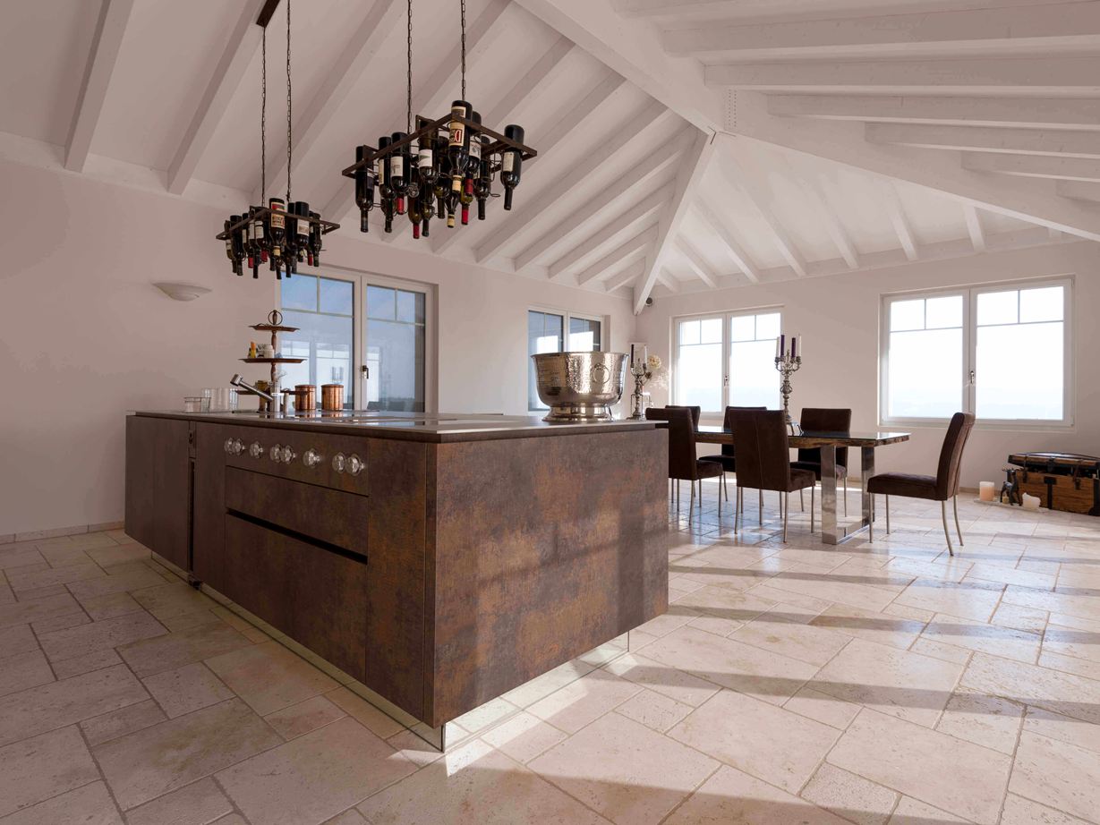 Kookeiland met wijnfleshouder aan het plafond, eettafel en stoelen op de achtergrond op gelegd Travertin Light met getrommeld, ongeslepen oppervlak Kookeiland met wijnfleshouder aan het plafond, op de achtergrond eettafel en stoelen op gelegd Travertin Light met getrommeld, niet geëgaliseerd oppervlak