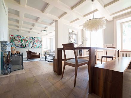 Moderne woon- en eetkamer met hoge, witte plafonds, houten vloer en een modern schilderij op de achtergrond