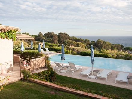 Een zwembad met witte ligstoelen en travertijnplaten, met de zee op de achtergrond