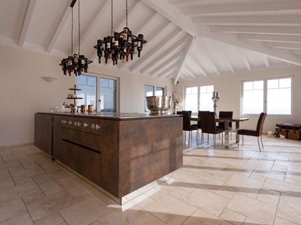 Kookeiland met wijnfleshouder aan het plafond, op de achtergrond eettafel en stoelen op gelegd Travertin Light met getrommeld, niet geëgaliseerd oppervlak