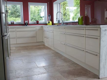 Klantenfoto van een keuken met witte meubels, rode muren en beigebruine travertin tegels