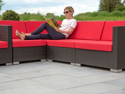 Vrouw zittend op moderne bank met rode kussens op een blauw terras