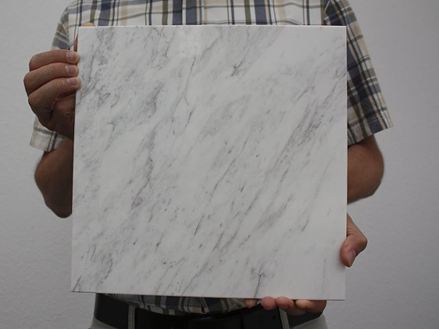 Persoon houdt een witte marmeren tegel met grijze aderen omhoog naar de camera