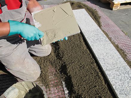 De installateur smeert de achterkant van de steen in met lijm voor het leggen met eenkorrelige mortel op steenslag draaglaag